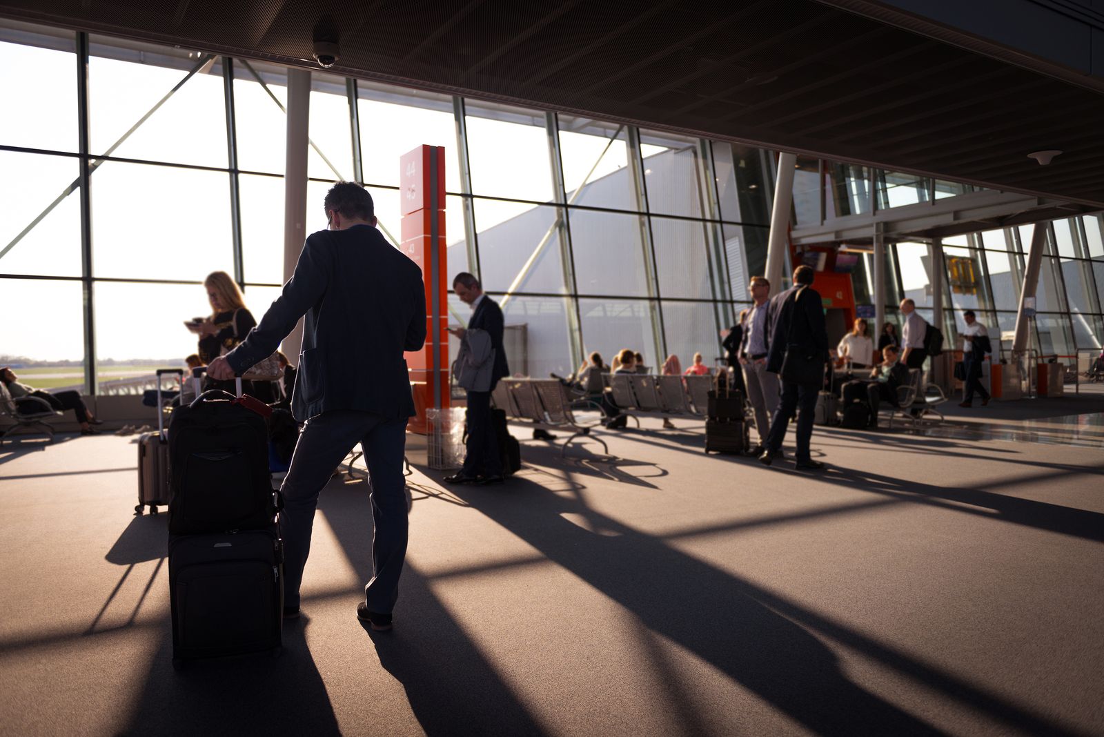 Travellers with carry-on bags crossing a sunlit airport terminal